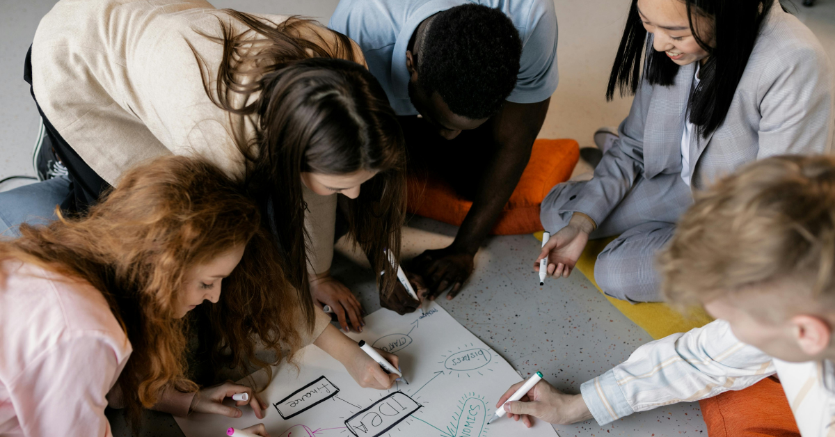 A diverse team gather round a large page with pens, mapping the steps need to achieve success.